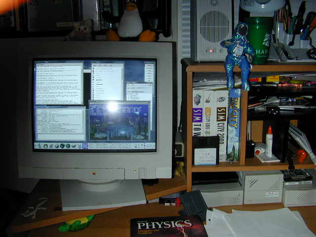A desk in 2000: an Apple CRT monitor running a Linux desktop with GtkHx
                  open — chat, user list, and a server banner visible — a Tux penguin plush
                  on top of the monitor, SimCity boxes on the shelf, and a physics textbook
                  in the foreground.